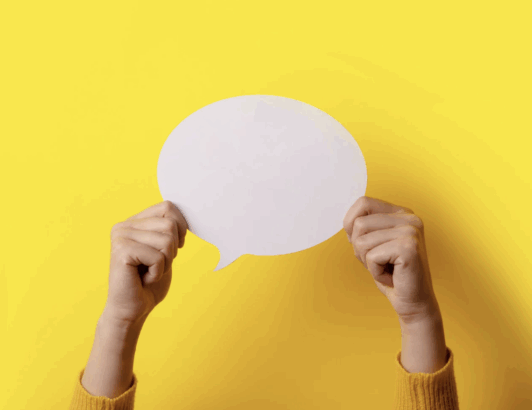 Hands holding blank white speech bubble against bright yellow background, symbolizing communication, messaging, or ideas.